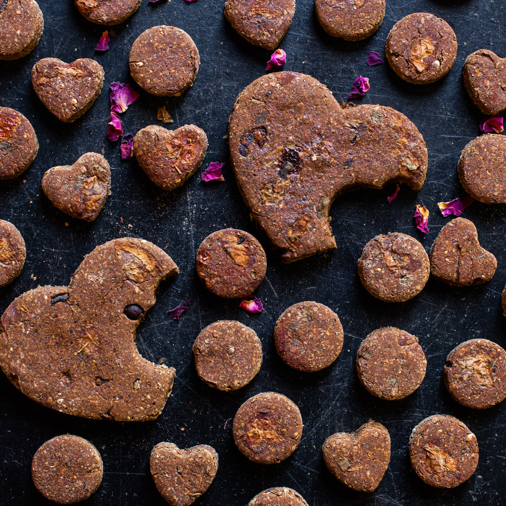 Hondenkoekjes in hartvorm met rozenbottel en rozenblaadjes er omheen
