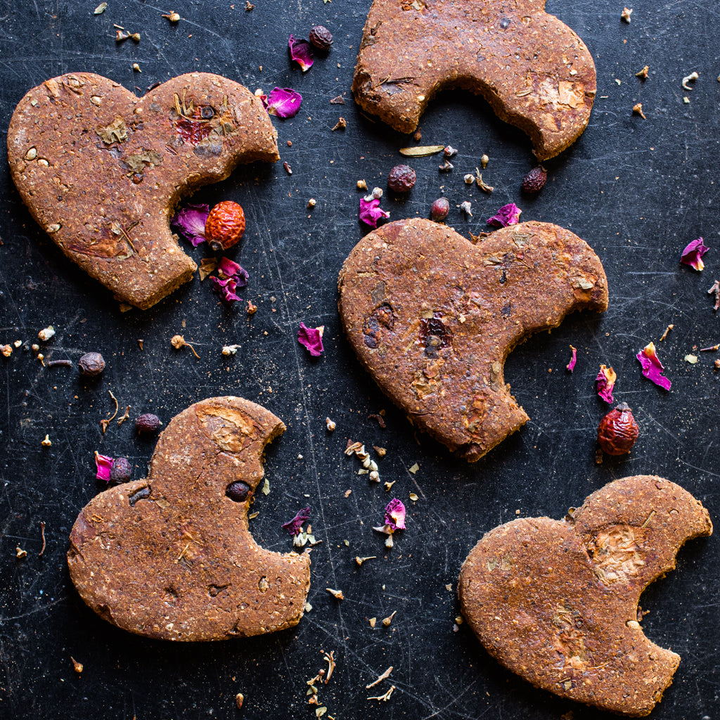 Hondenkoekjes in hartvorm met rozenbottel en rozenblaadjes er omheen